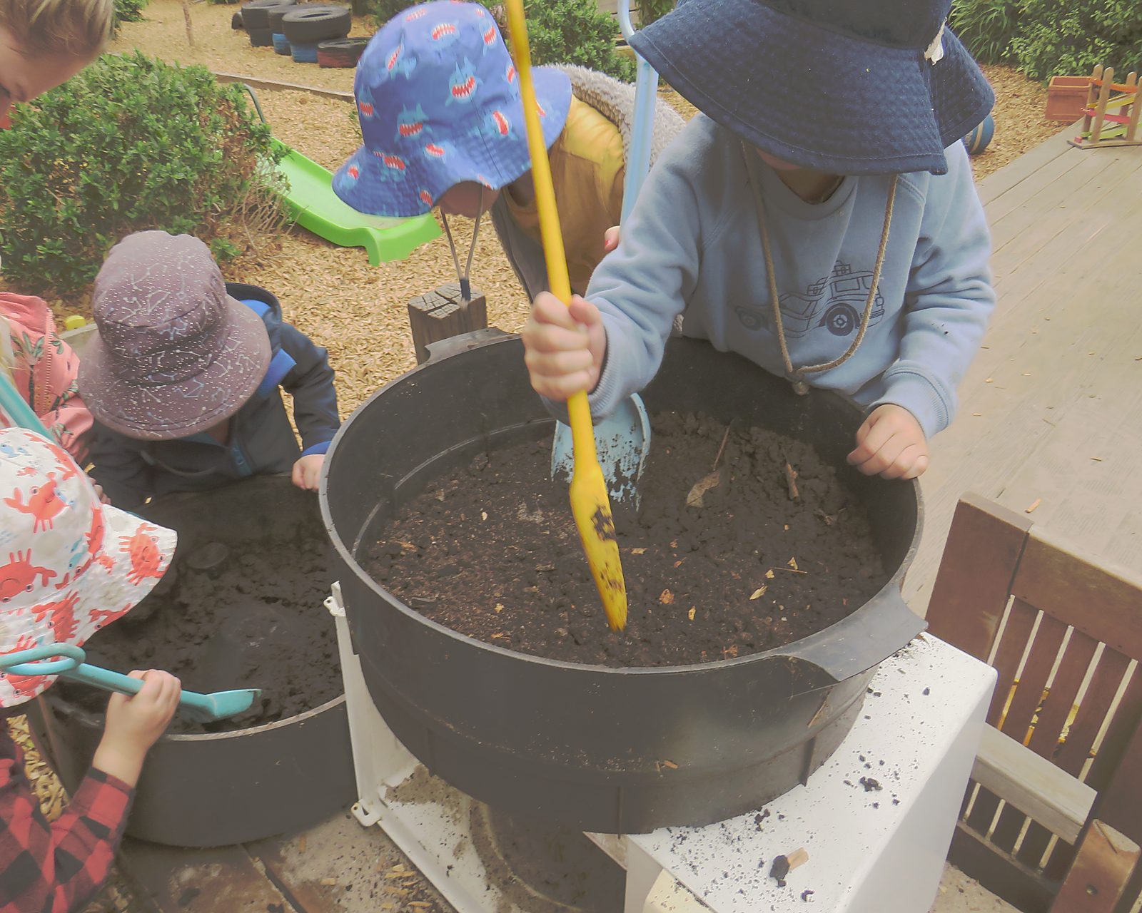 Children mixing soil in the Kinderclub garden, hands and natural materials at the centre of play