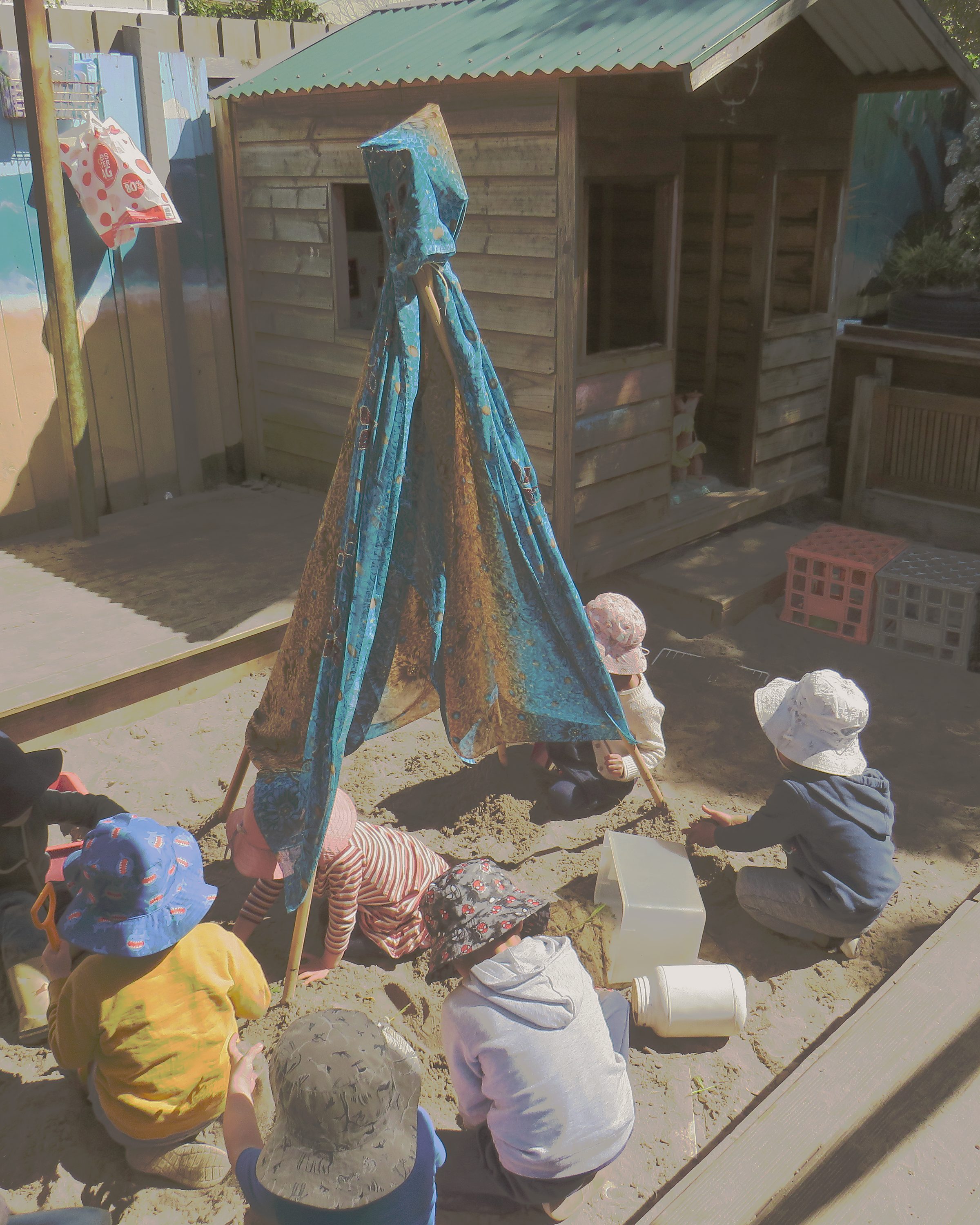 Children playing in the Kinderclub sandpit beneath a handmade teepee